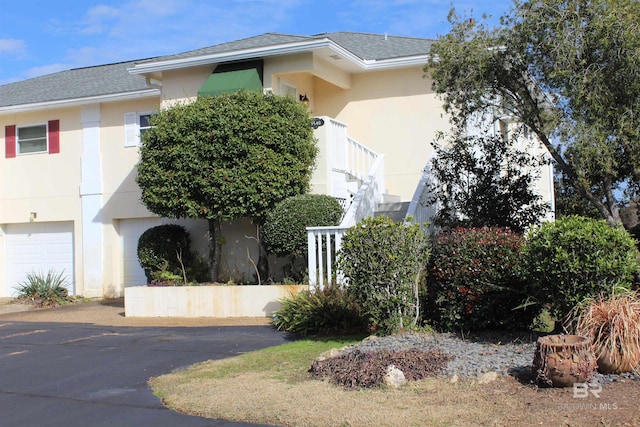 exterior space featuring stucco siding, an attached garage, a shingled roof, and stairs