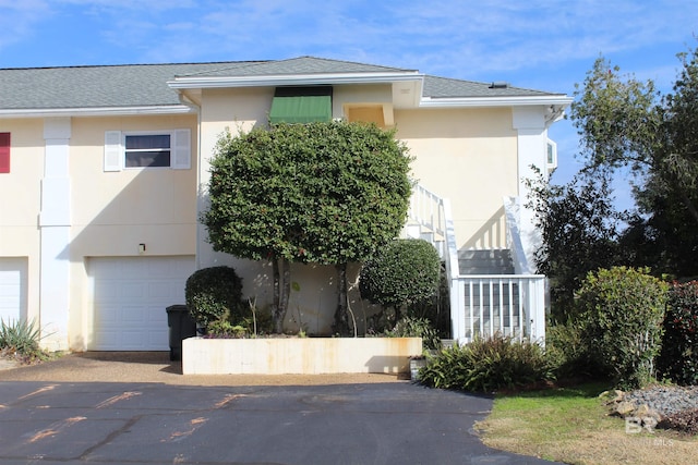 view of front of property featuring stucco siding, stairs, a garage, and roof with shingles