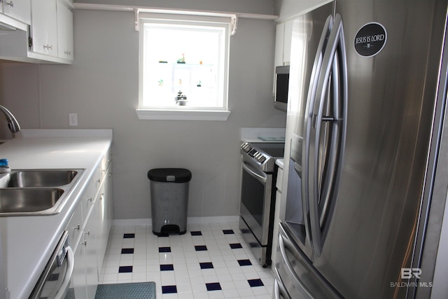 kitchen with baseboards, light countertops, white cabinets, stainless steel appliances, and a sink