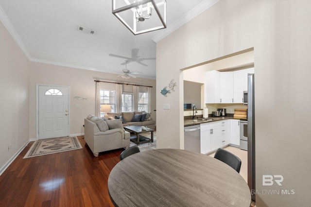 dining room with sink, dark wood-type flooring, ceiling fan with notable chandelier, and ornamental molding