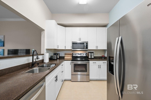 kitchen with dark stone counters, white cabinets, sink, ornamental molding, and stainless steel appliances