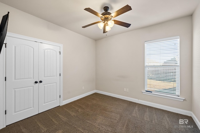 unfurnished bedroom featuring multiple windows, a closet, dark carpet, and ceiling fan