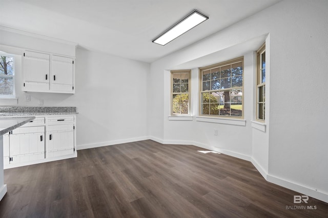 unfurnished dining area with dark wood-type flooring and baseboards