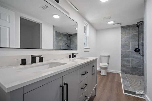 full bath with visible vents, toilet, a sink, wood finished floors, and tiled shower