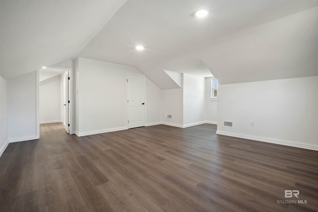 additional living space with dark wood-style floors, baseboards, visible vents, and vaulted ceiling