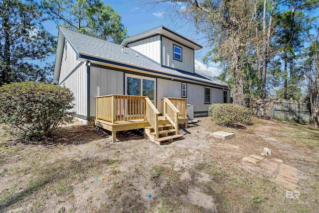 back of house with a deck, roof with shingles, and fence