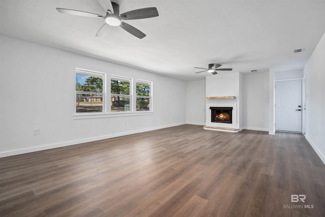 unfurnished living room with dark wood-style floors, visible vents, a ceiling fan, a warm lit fireplace, and baseboards