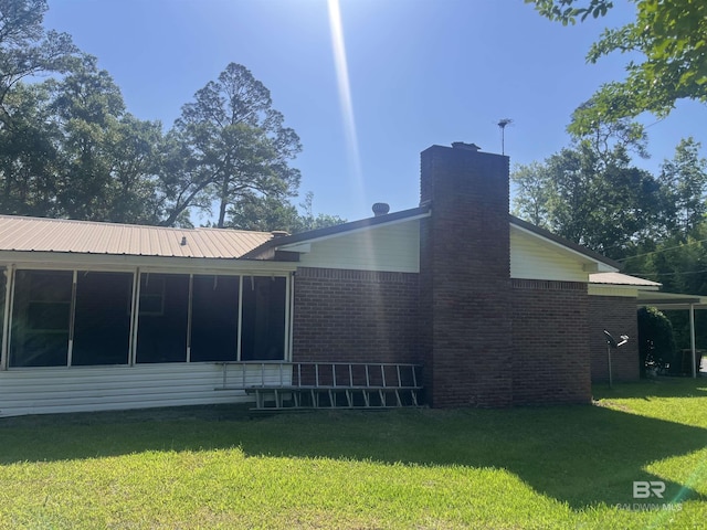 rear view of house with a chimney, brick siding, a yard, and a sunroom