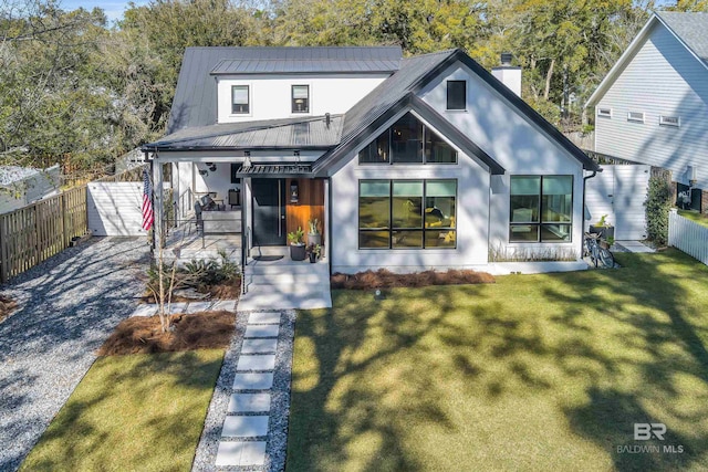 modern farmhouse with metal roof, covered porch, fence, a chimney, and a front yard