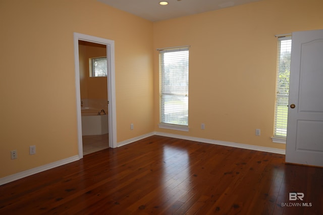 spare room featuring a wealth of natural light, baseboards, and dark wood finished floors