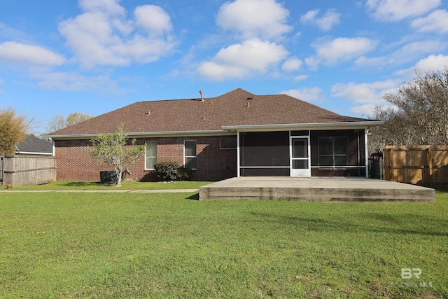 rear view of property featuring brick siding, a shingled roof, fence, a lawn, and a sunroom