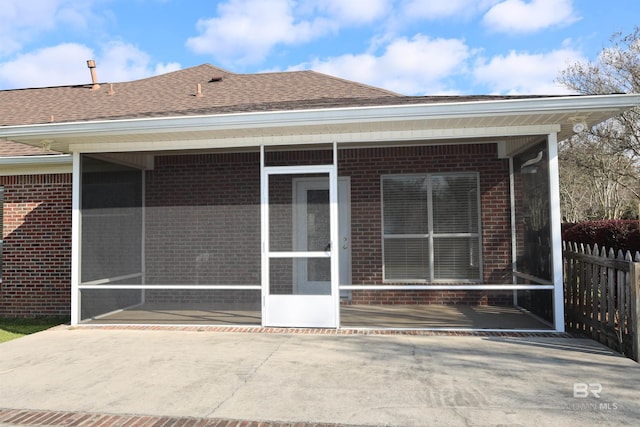 back of house featuring brick siding, roof with shingles, and a sunroom