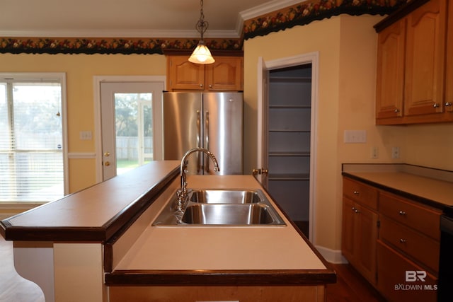 kitchen with a kitchen island with sink, ornamental molding, a sink, decorative light fixtures, and freestanding refrigerator