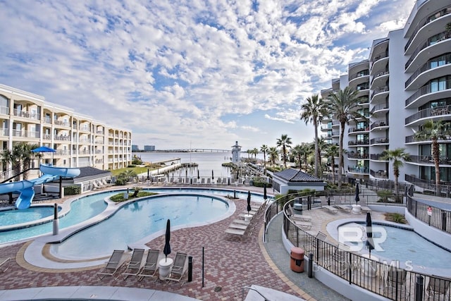 pool featuring a water slide, a patio area, fence, and a water view