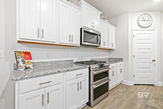 kitchen with white cabinets, light wood-type flooring, stainless steel appliances, and light stone countertops