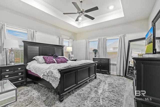 bedroom with hardwood / wood-style floors, ceiling fan, crown molding, and a tray ceiling