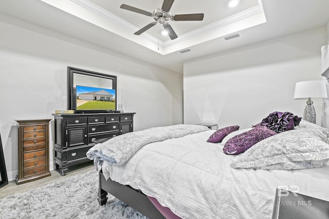 bedroom with a tray ceiling, ceiling fan, light wood-type flooring, and ornamental molding