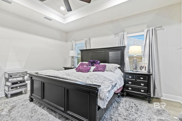 bedroom with hardwood / wood-style flooring, ceiling fan, a raised ceiling, and crown molding