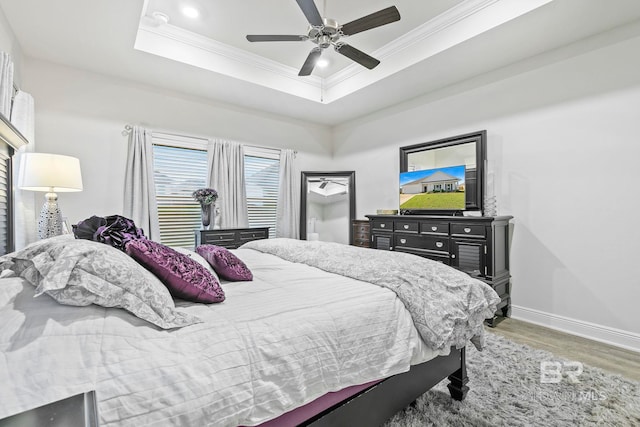 bedroom featuring hardwood / wood-style flooring, ceiling fan, ornamental molding, and a tray ceiling