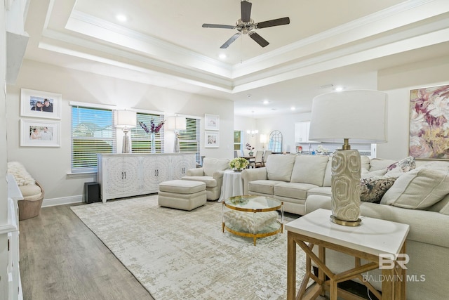 living room featuring ceiling fan with notable chandelier, wood-type flooring, ornamental molding, and a tray ceiling