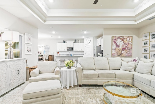 living room with ceiling fan, a raised ceiling, and ornamental molding