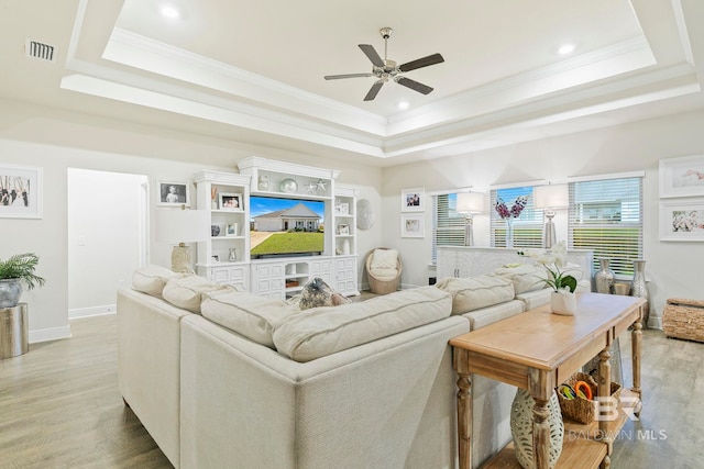 living room with light wood-type flooring, a raised ceiling, ceiling fan, and crown molding