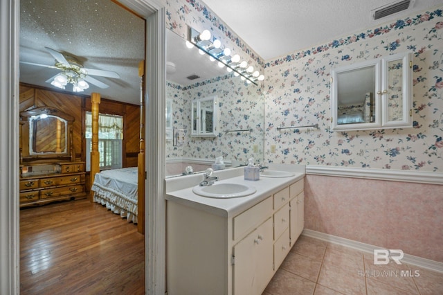 bathroom featuring a textured ceiling, wood-type flooring, ceiling fan, and dual bowl vanity