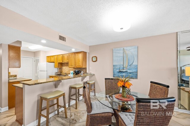 kitchen featuring white fridge, kitchen peninsula, a breakfast bar, stone countertops, and backsplash