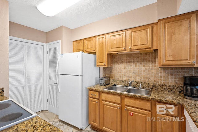 kitchen featuring white fridge, dark stone countertops, backsplash, and sink