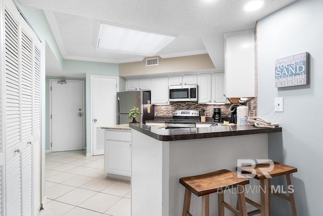 kitchen featuring appliances with stainless steel finishes, white cabinets, backsplash, a breakfast bar area, and kitchen peninsula