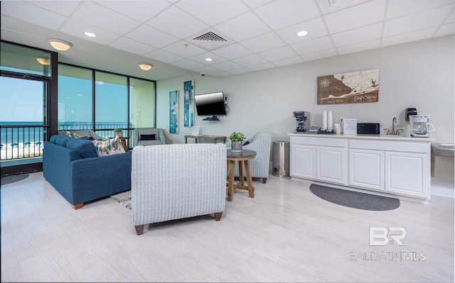 living room featuring floor to ceiling windows, a water view, sink, and a drop ceiling