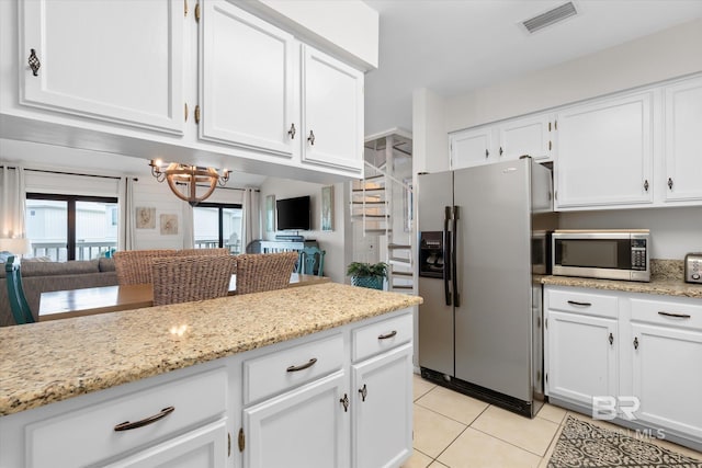 kitchen with appliances with stainless steel finishes, white cabinets, light tile patterned floors, a notable chandelier, and light stone counters