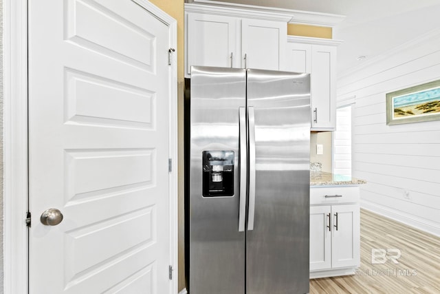 kitchen featuring wooden walls, white cabinets, stainless steel fridge, light stone countertops, and light hardwood / wood-style flooring