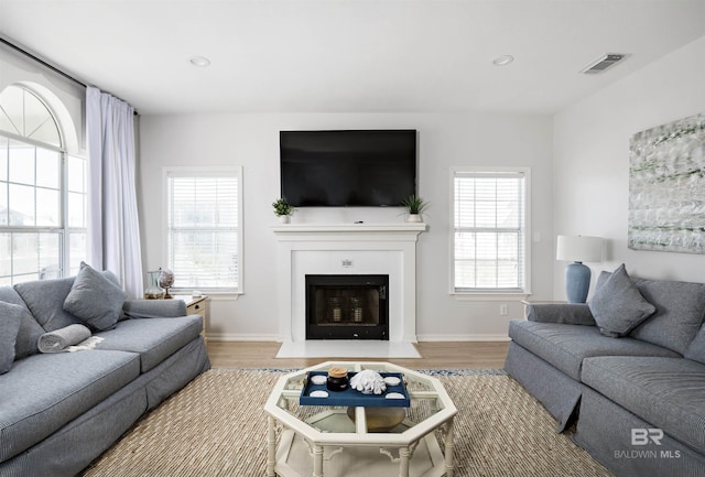 living room featuring a fireplace with flush hearth, recessed lighting, visible vents, and wood finished floors