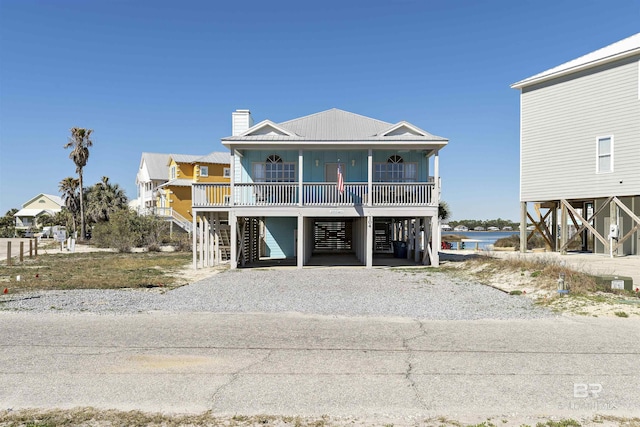 coastal home with a chimney, stairway, gravel driveway, a porch, and a carport