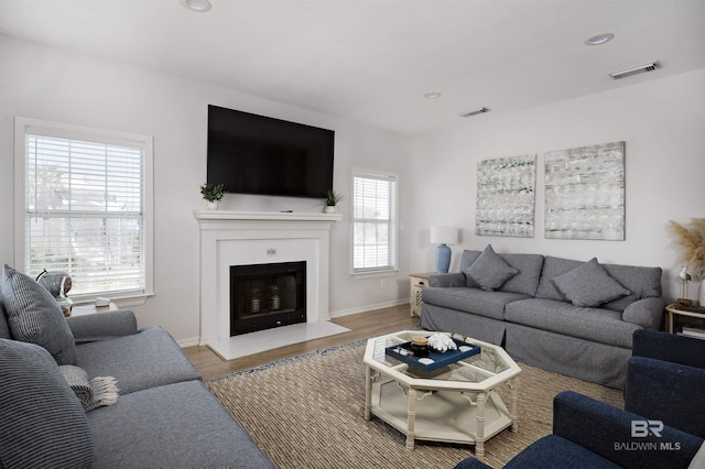 living area featuring a fireplace with flush hearth, visible vents, wood finished floors, and recessed lighting