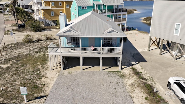 rear view of house with board and batten siding, a chimney, a water view, gravel driveway, and a carport