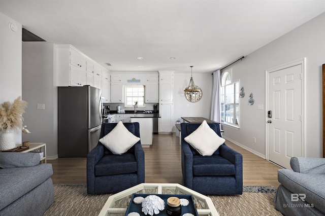 living room with a notable chandelier, recessed lighting, light wood-style flooring, and baseboards