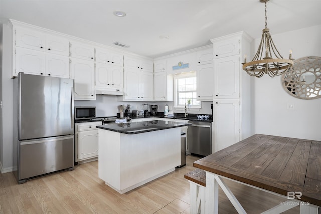 kitchen with a center island, stainless steel appliances, dark countertops, white cabinets, and light wood-type flooring