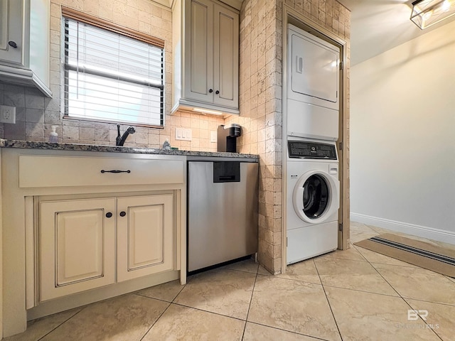 laundry area with light tile patterned floors, stacked washer / drying machine, baseboards, and a sink