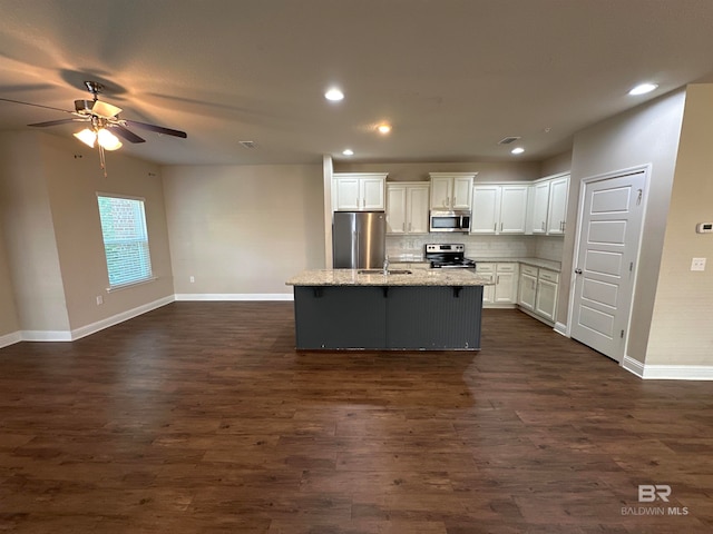 kitchen featuring a center island with sink, white cabinets, appliances with stainless steel finishes, light stone counters, and dark hardwood / wood-style flooring