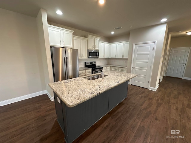 kitchen with white cabinets, stainless steel appliances, light stone counters, and an island with sink