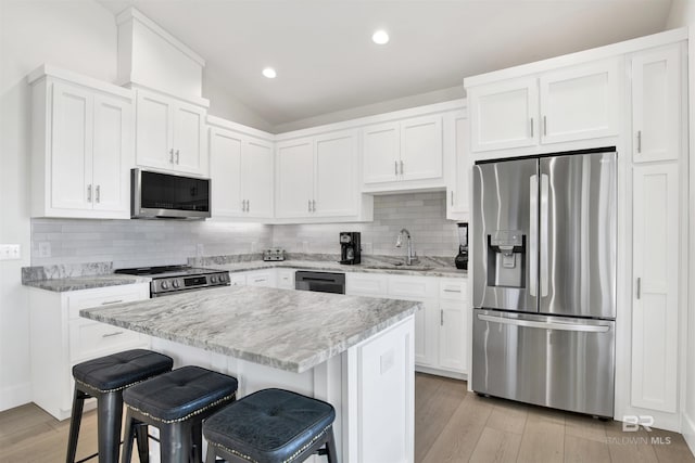 kitchen with lofted ceiling, a breakfast bar area, stainless steel appliances, light wood-type flooring, and a sink