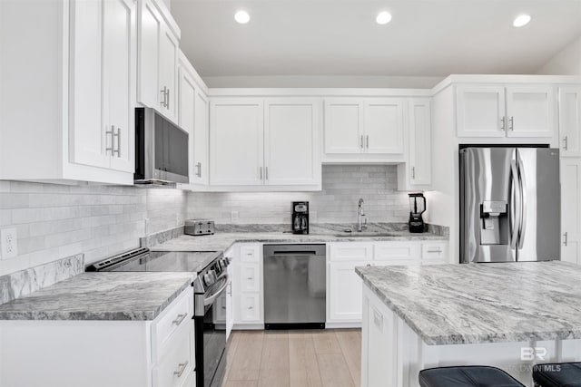 kitchen featuring light wood-style flooring, stainless steel appliances, a sink, white cabinets, and light stone countertops