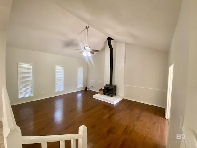 unfurnished living room featuring a ceiling fan, baseboards, dark wood-style flooring, a wood stove, and lofted ceiling