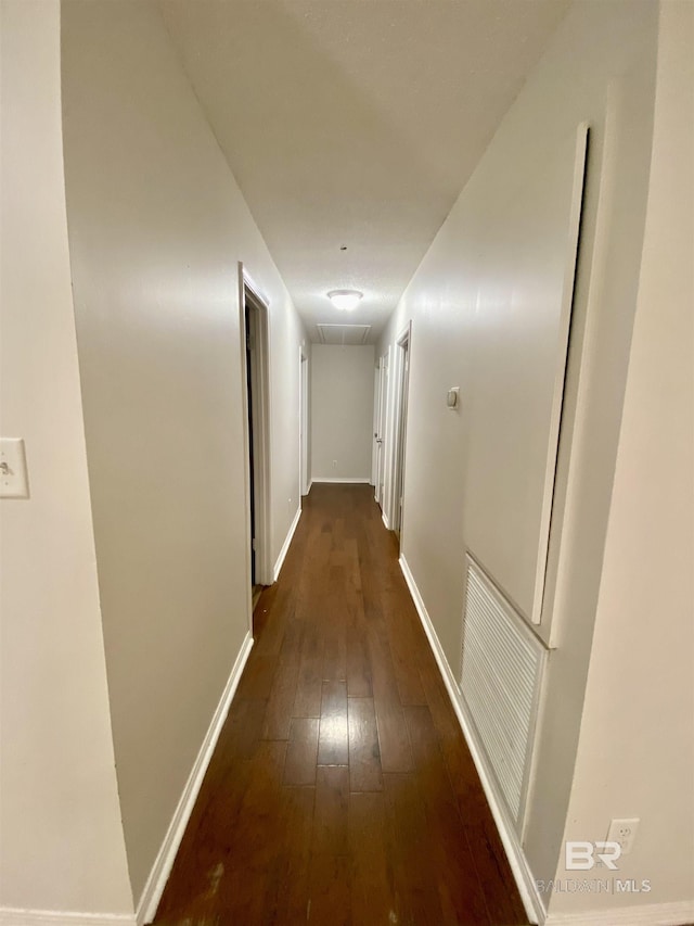 hallway with baseboards, visible vents, attic access, and dark wood-type flooring