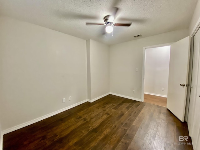 spare room with a textured ceiling, dark wood-type flooring, visible vents, a ceiling fan, and baseboards