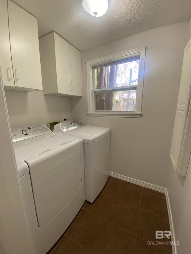 laundry room with a textured ceiling, baseboards, dark tile patterned floors, washer and clothes dryer, and cabinet space