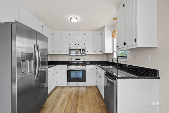 26498 Carondelette Dr, Orange Beach, AL 36561 - kitchen with appliances with stainless steel finishes, a sink, light wood-type flooring, dark stone counters, and white cabinetry