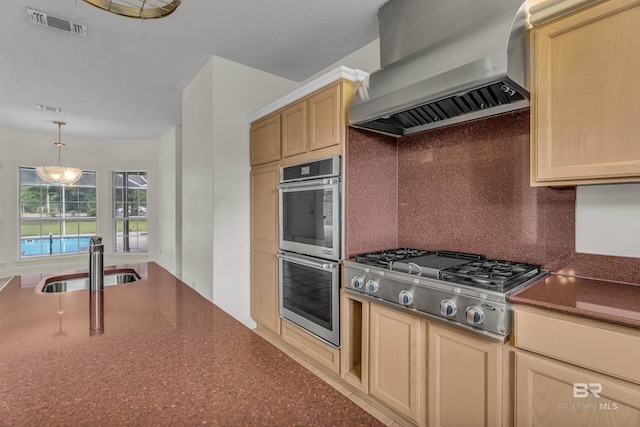 kitchen with wall chimney range hood, decorative backsplash, visible vents, appliances with stainless steel finishes, and a sink